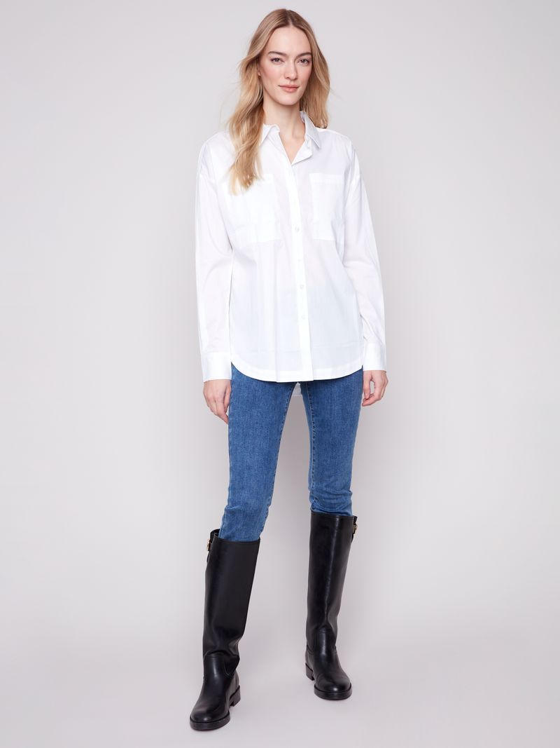 Woman wearing a white shirt, blue jeans, and black boots on a plain background