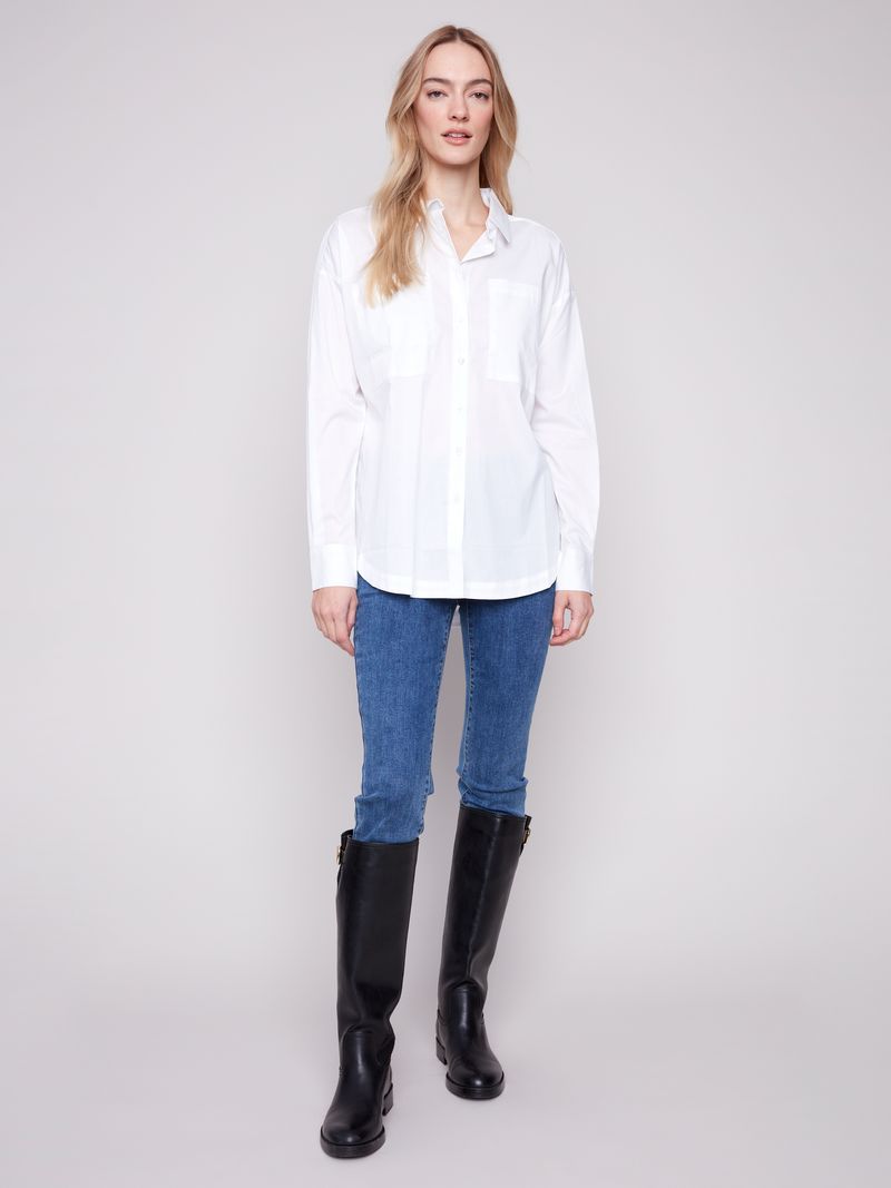 Woman wearing a white shirt, blue jeans, and black knee-high boots on a plain background