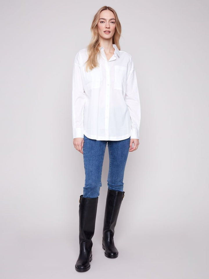 Woman wearing a white shirt, blue jeans, and black knee-high boots on a plain background