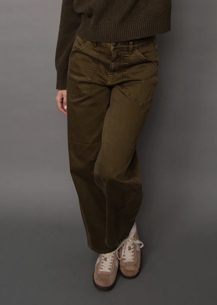 A person wearing olive green wide-leg cargo pants, a dark brown ribbed sweater, and beige sneakers, standing against a solid gray studio background.