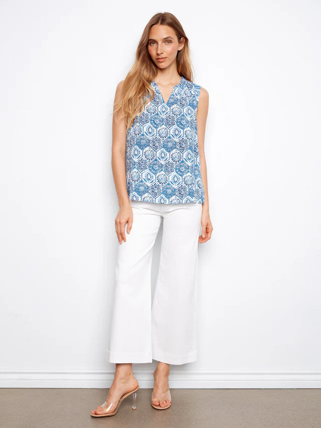 Woman wearing a blue floral top and white pants against a white background