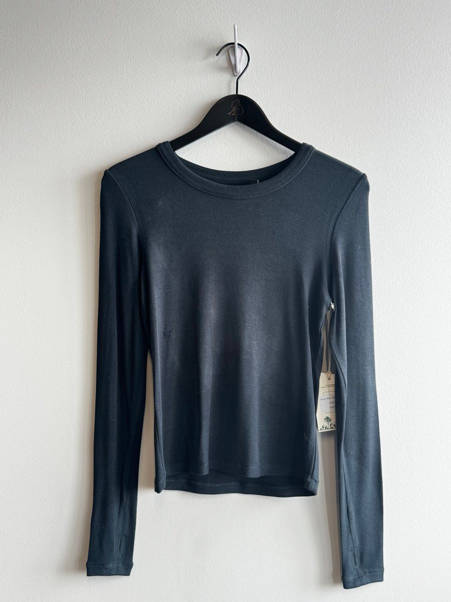 A dark slate blue long-sleeve crewneck top hanging on a black hanger against a plain white wall.