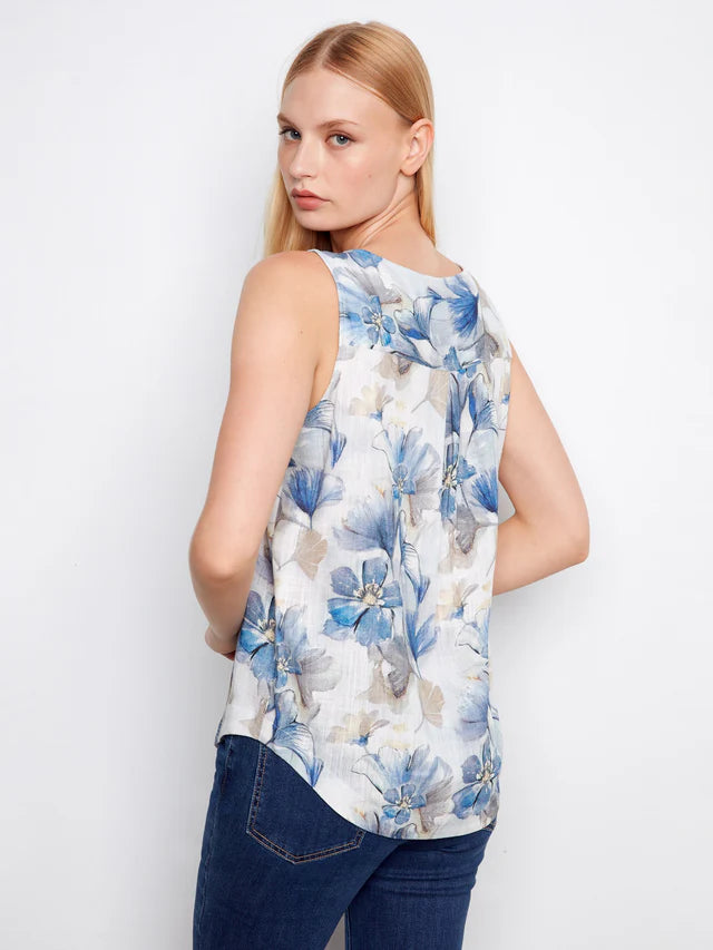 Woman wearing a sleeveless floral top with blue and white flowers on a plain background
