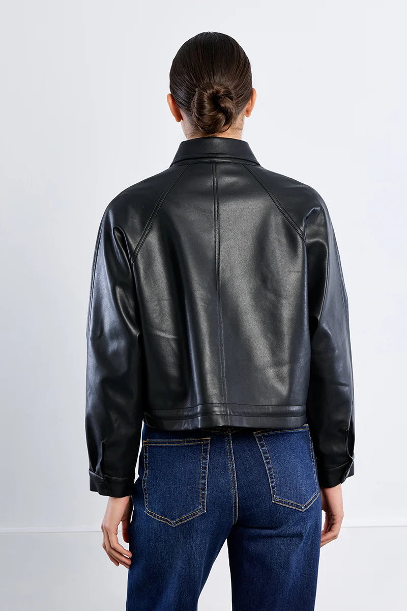 A person shown from the back wearing a black leather cropped jacket and blue jeans against a plain light gray studio background.