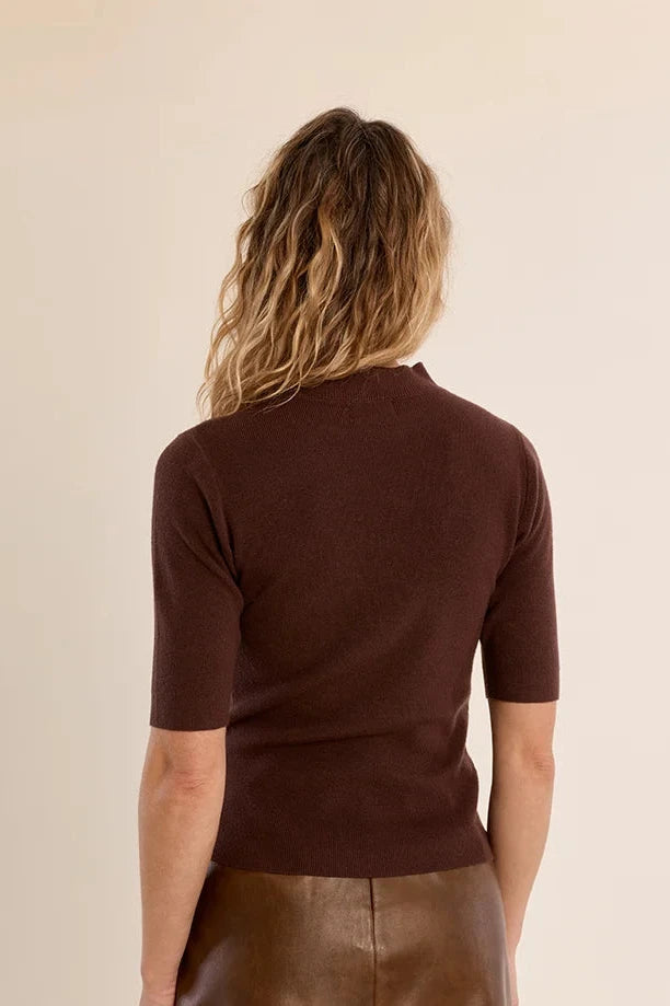 A woman shown from the back wearing a dark brown short-sleeve knit top and a brown faux-leather mini skirt, set against a plain beige studio background.