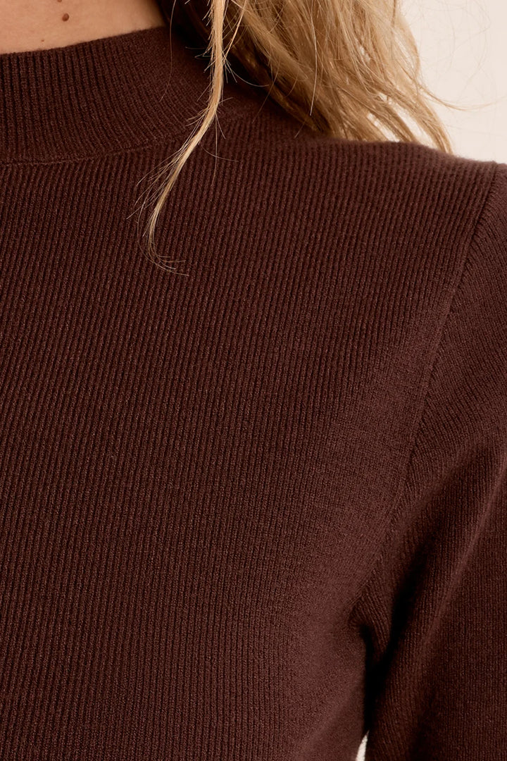 Close-up of a ribbed knit sweater in a deep chocolate brown color, worn by a model with blonde hair visible near the collar.