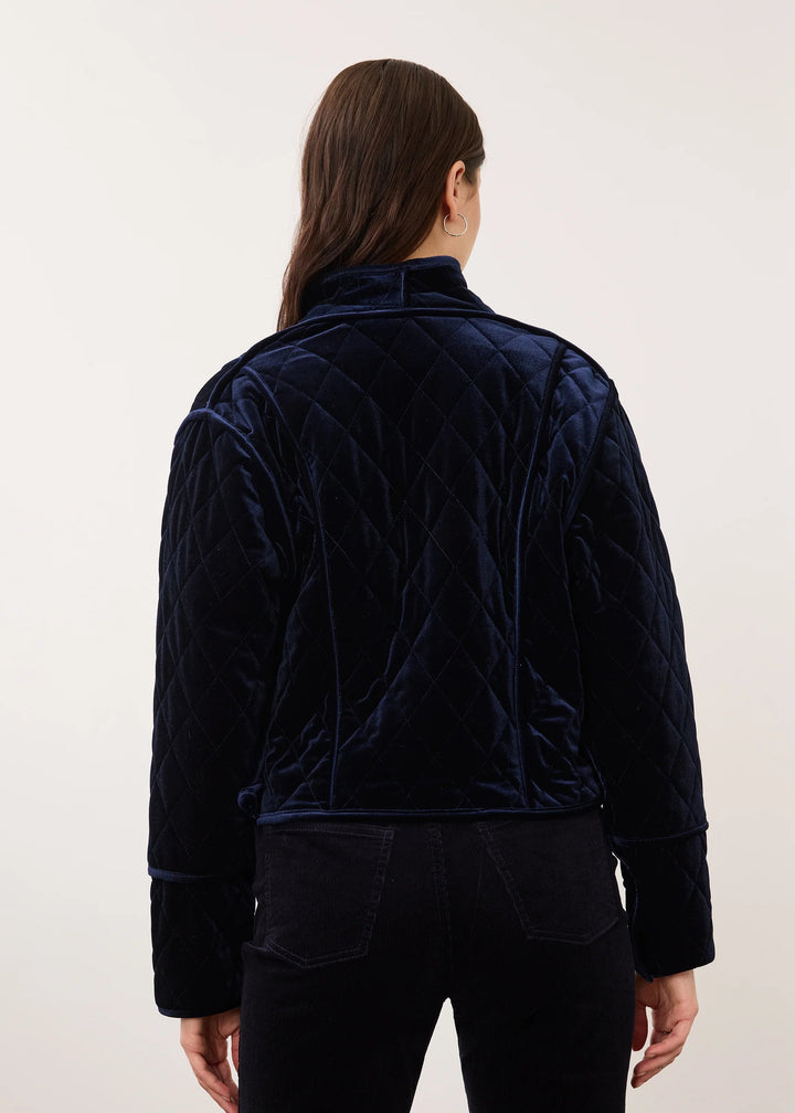 A model viewed from the back wearing a dark navy blue quilted velvet jacket and matching dark pants against a plain light background.