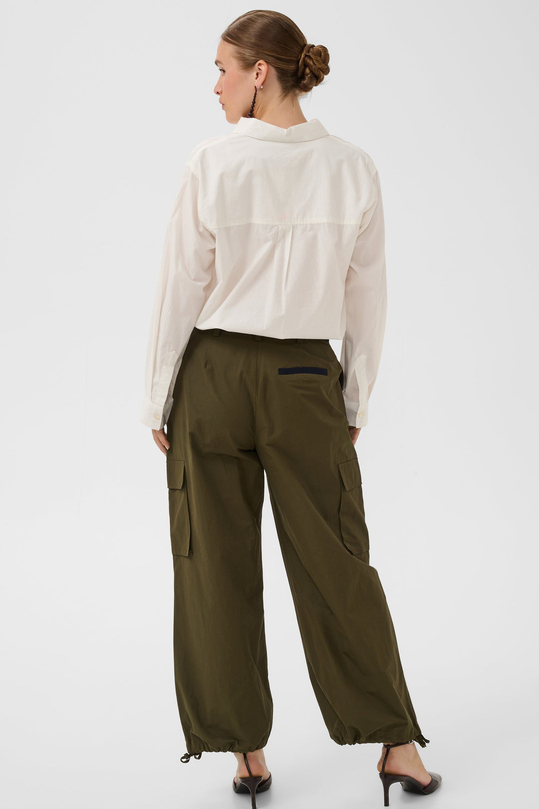 Woman wearing a white blouse and olive green pants on a white background