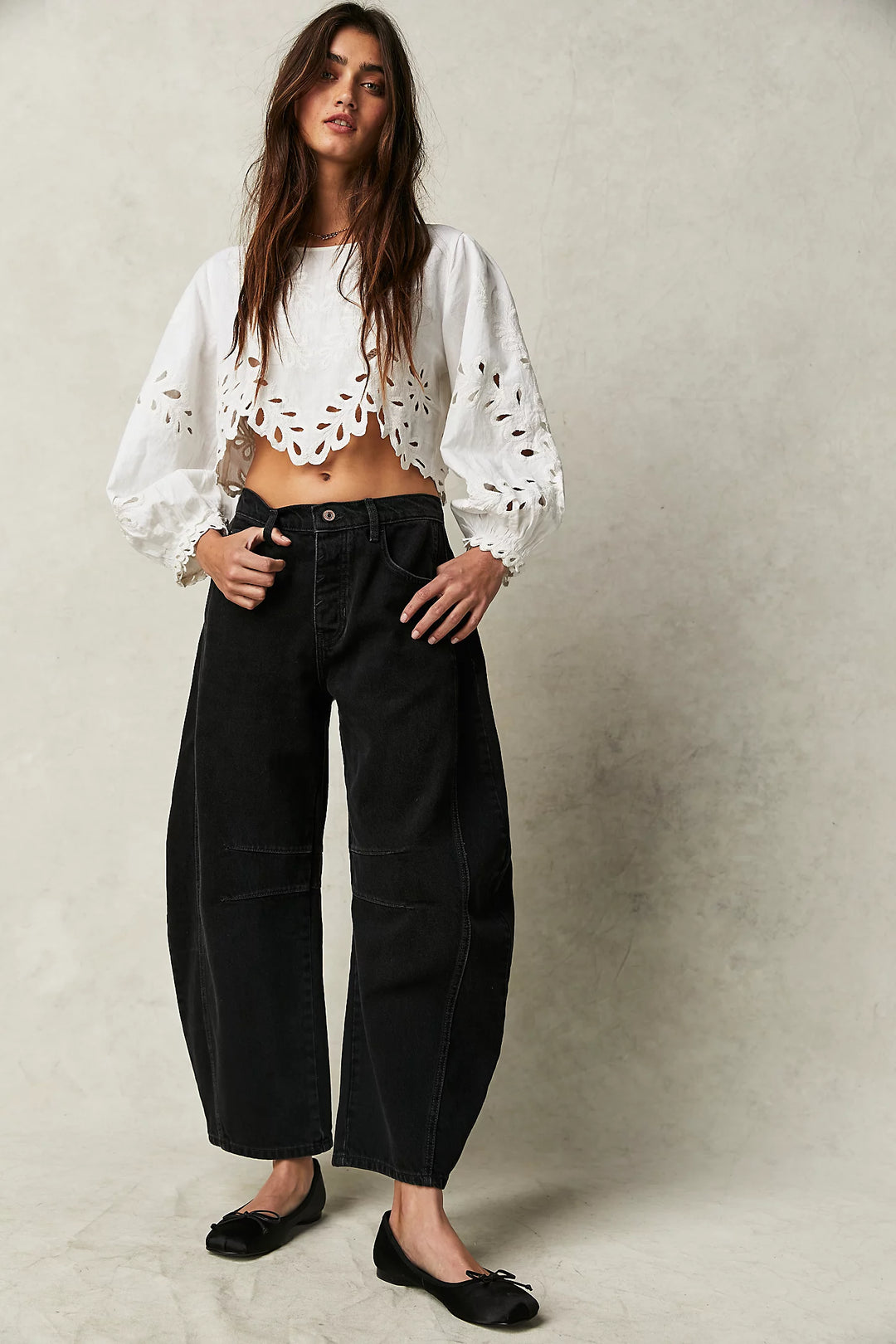Woman wearing a white blouse with cut-out details and black pants on a neutral background