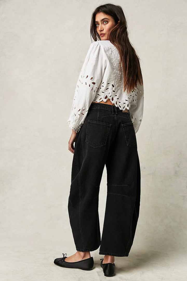 Woman wearing a white blouse with lace details and black pants on a plain background