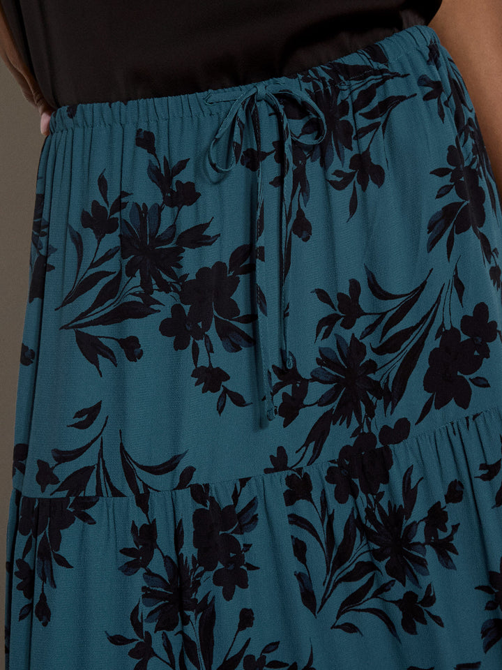 Close-up of a tiered skirt in teal blue with a black floral print and a drawstring waist, worn with a black top.