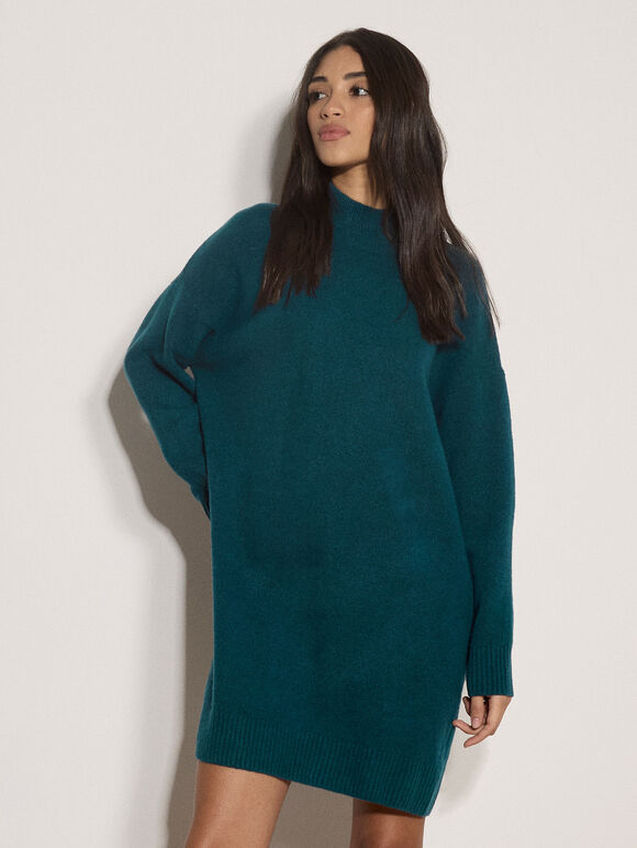A woman modeling an oversized dark teal knit sweater dress against a plain off-white background.