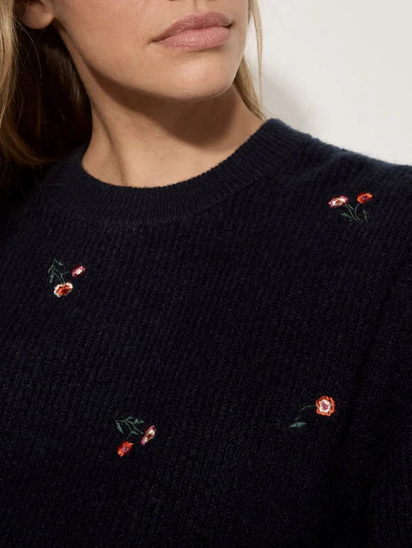 Close-up of a person wearing a dark navy knit sweater with small embroidered red and pink flowers and green leaves.