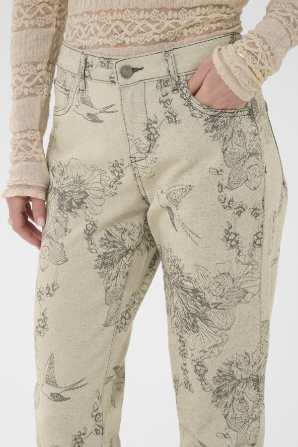 Beige pants with black floral patterns worn by a person on a white background