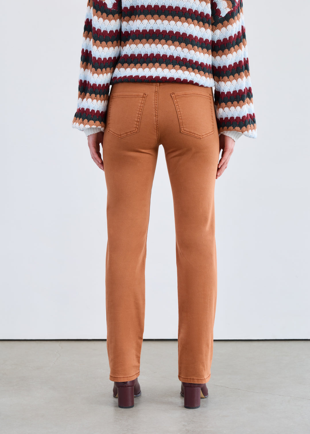 Person wearing brown pants and a multicolored striped sweater against a white background