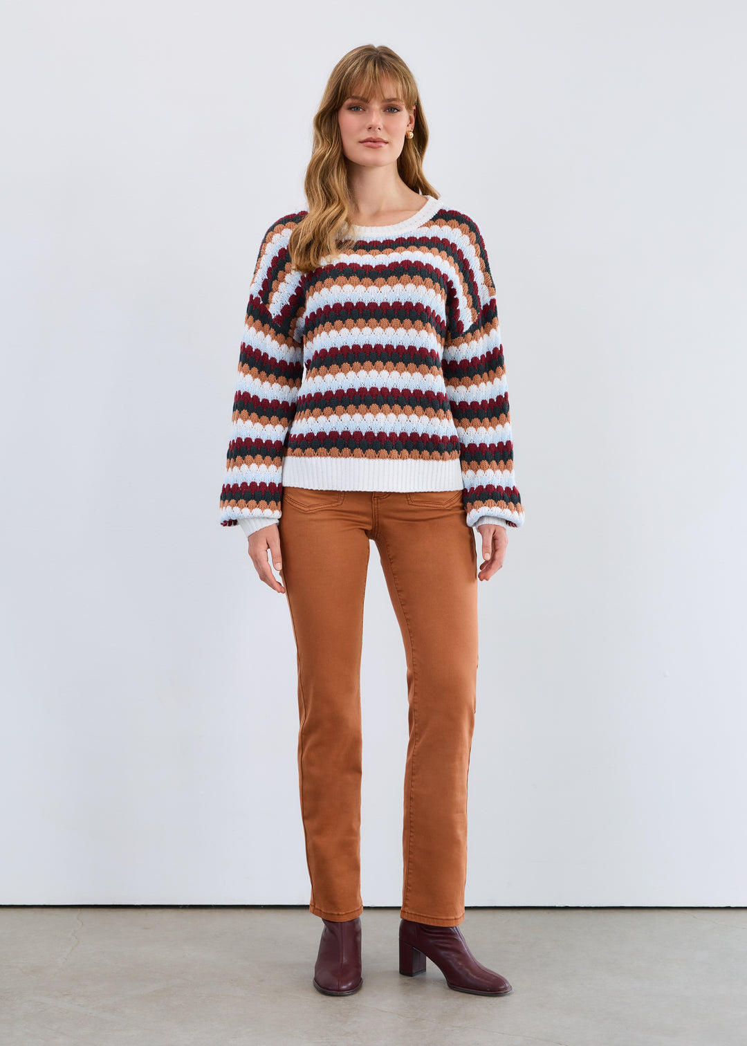 Woman wearing a striped sweater and brown pants against a white background