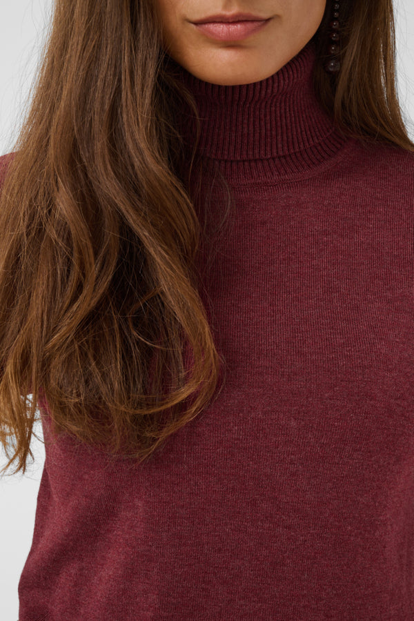 Close-up of a woman wearing a ribbed turtleneck sweater in a heathered burgundy color, with her hair and lower face visible against a light gray background.