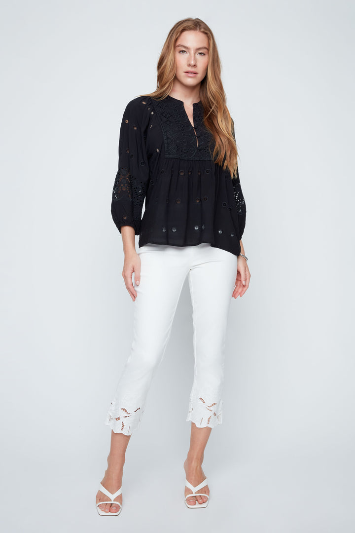 Woman wearing a black lace top and white pants on a light gray background