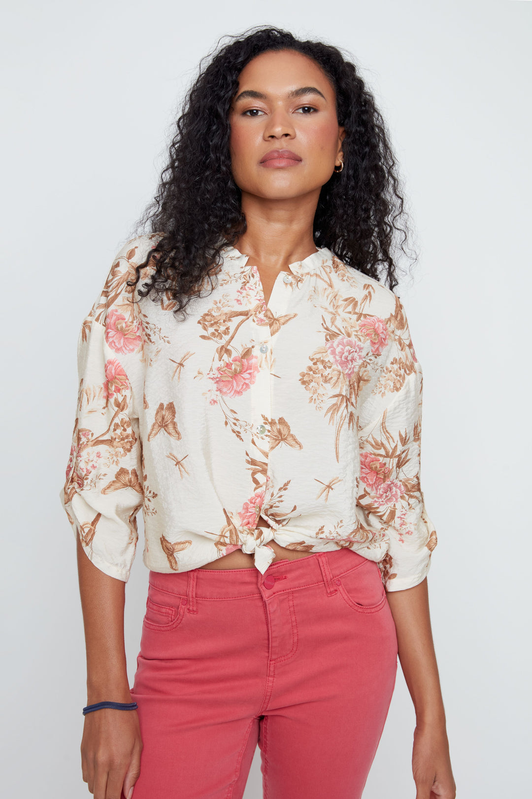 Woman wearing a floral blouse and pink pants against a white background