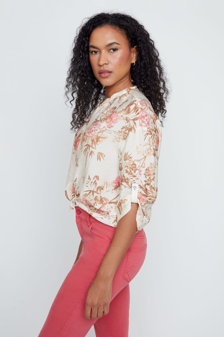 Woman wearing a floral blouse and pink pants against a white background