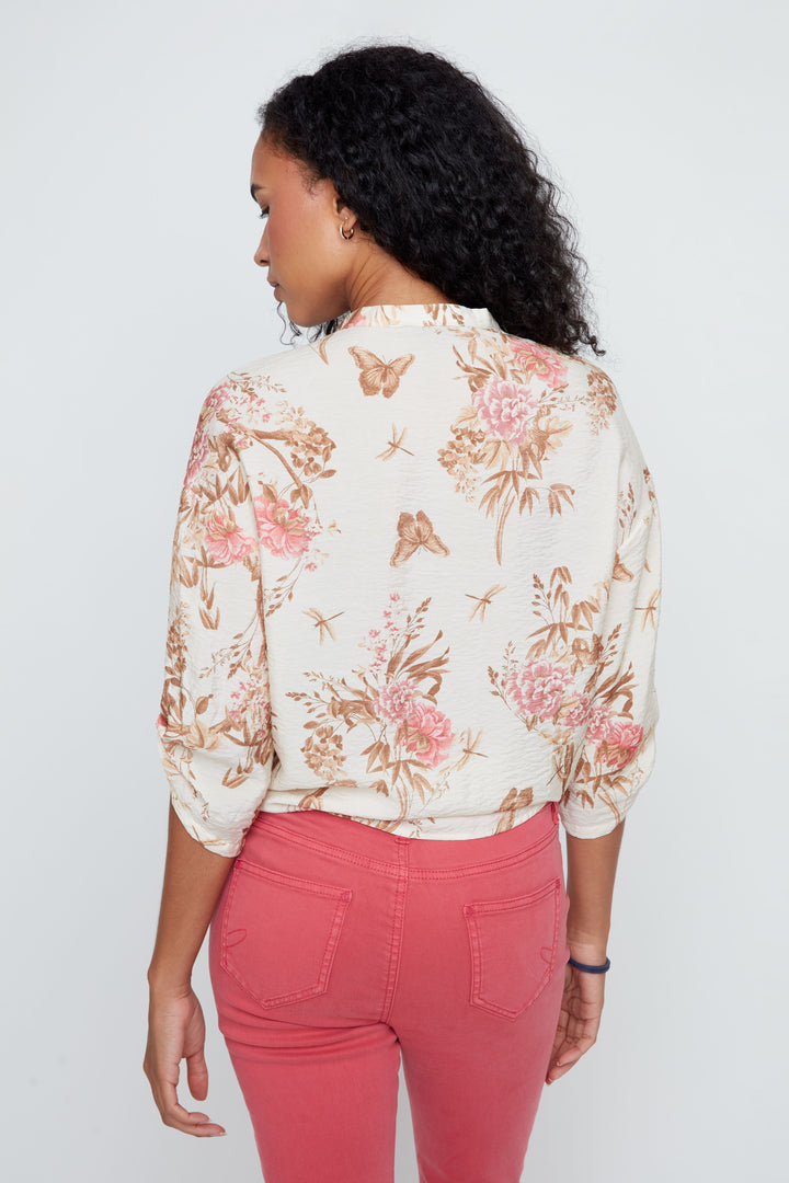 Woman wearing a floral blouse and pink pants against a white background