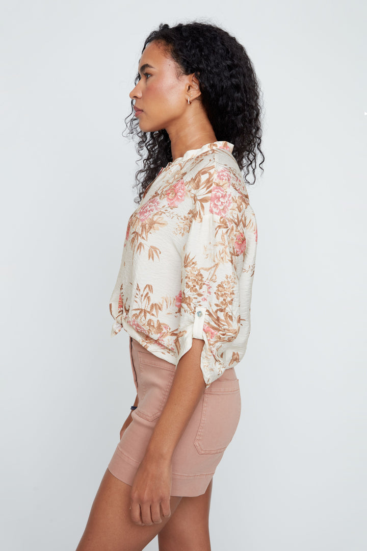 Woman wearing a floral blouse and beige shorts against a white background