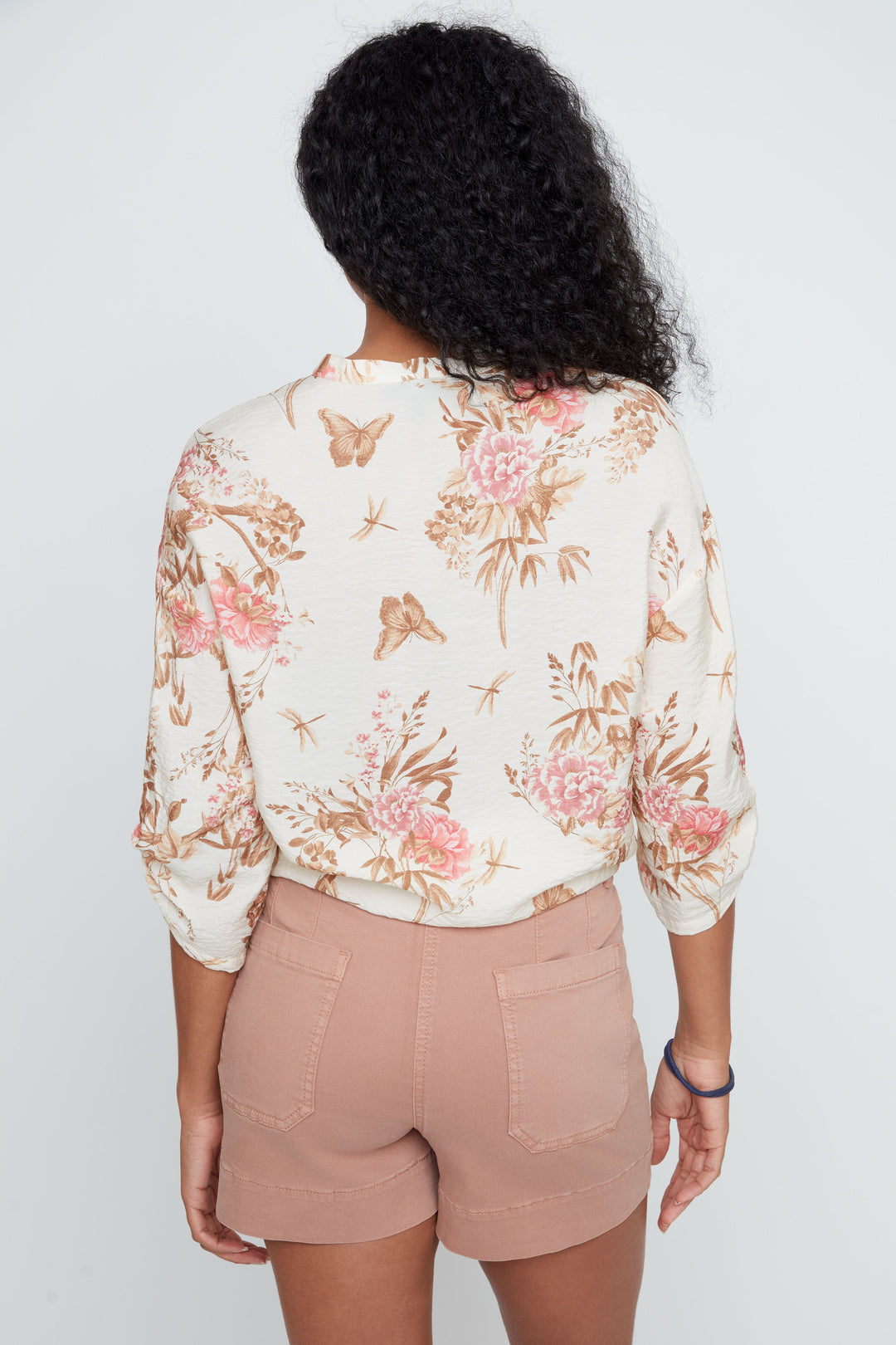 Person wearing a floral blouse and beige shorts on a plain background