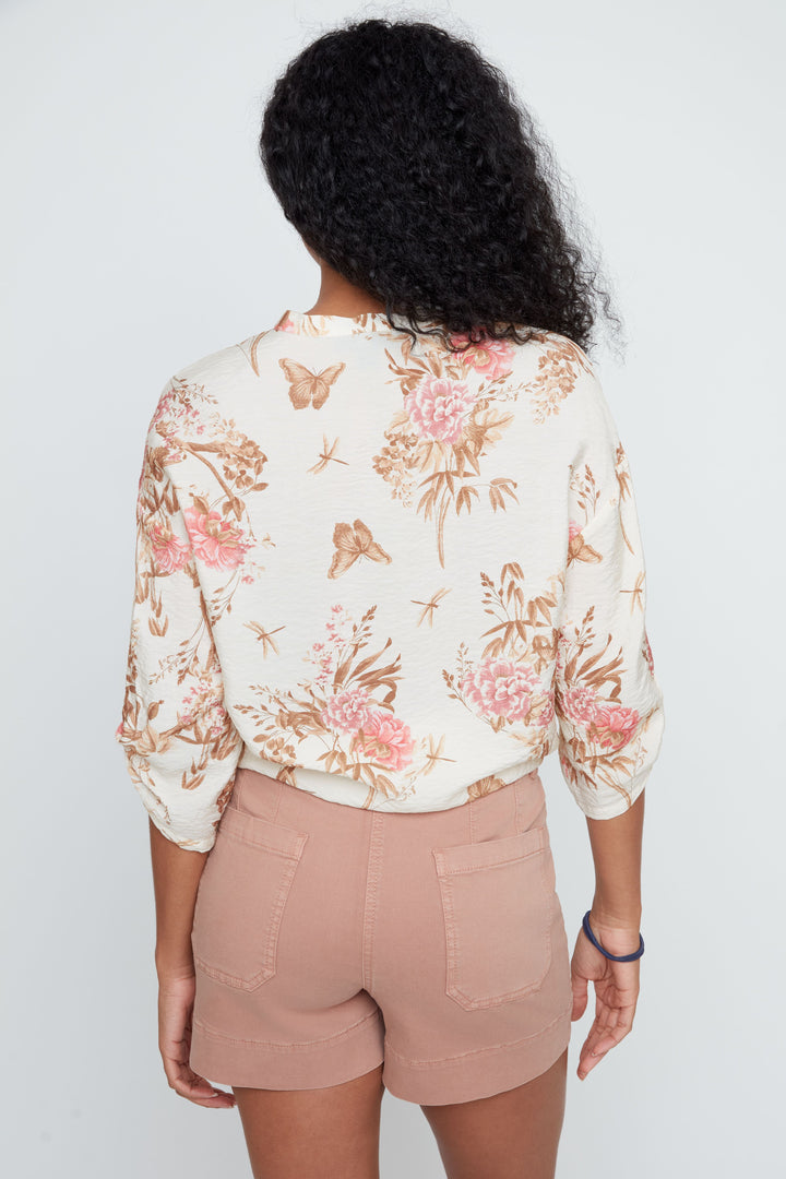 Person wearing a floral blouse and beige shorts on a plain background