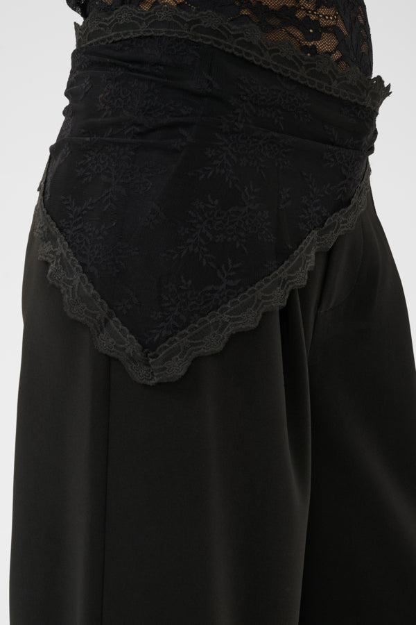 Close-up of a black skirt with a lace-trimmed waistband and a draped lace panel over the back, shown against a plain light background.