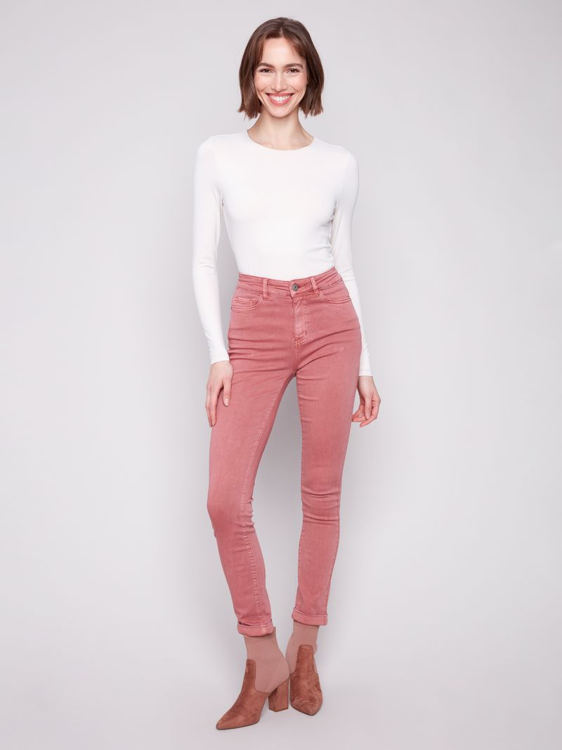 Woman wearing pink jeans and a white top on a plain background