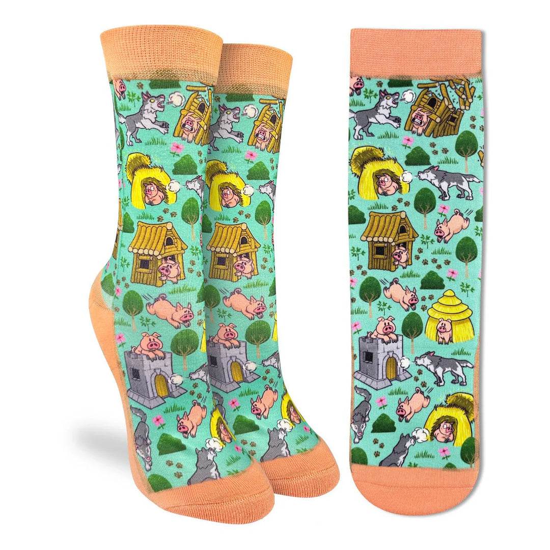 A pair of crew socks shown from the front and side on a white background. The socks feature a light mint green background with a whimsical cartoon pattern of pigs in houses, dogs, cats, and a woman in a yellow sunhat.