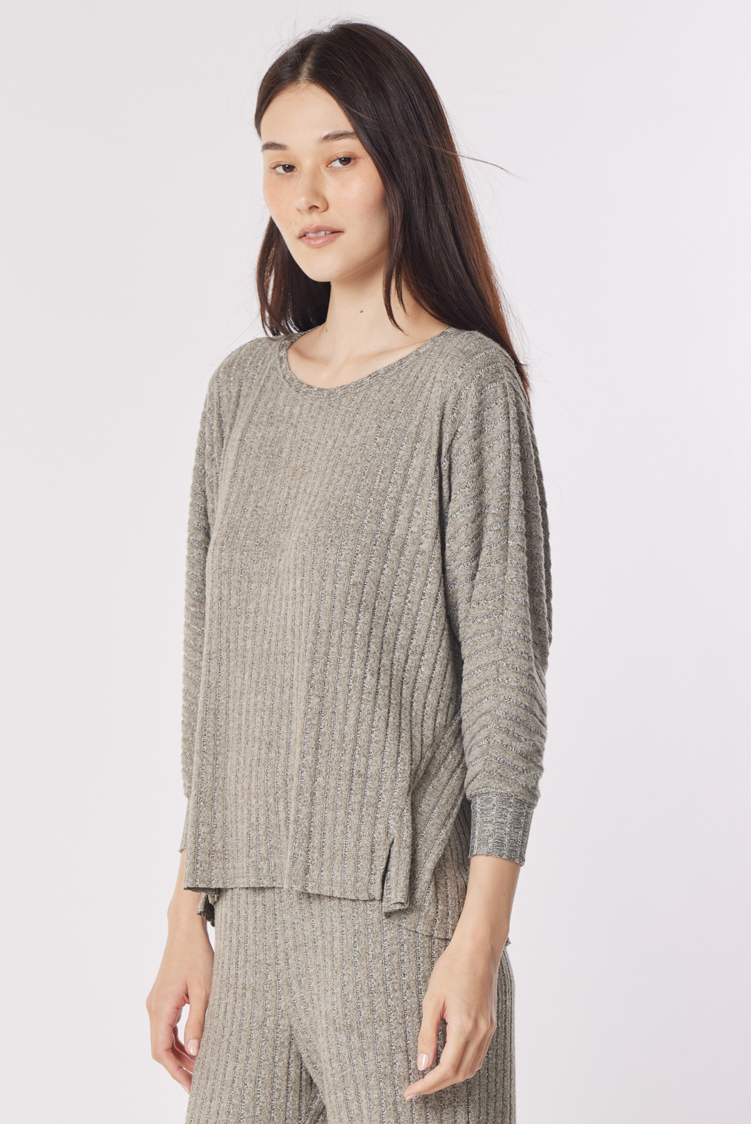 A woman modeling a ribbed knit long-sleeve top and matching pants in a heathered taupe-gray color, photographed against a plain light gray studio background.