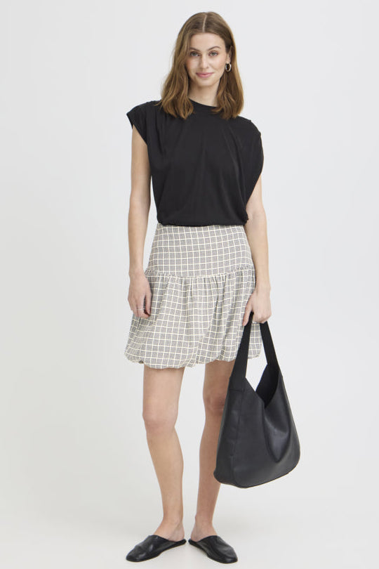 Woman wearing a black top and checkered skirt holding a black bag on a white background