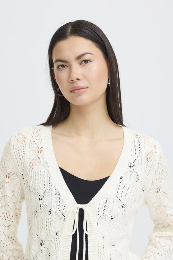 Woman wearing a white lace cardigan over a black top against a plain background