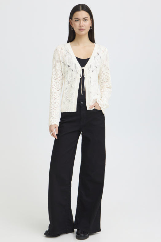 Woman wearing a white lace cardigan over a black top and pants on a white background