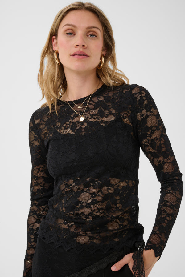 A woman wearing a black long-sleeve lace top with a crew neck, photographed against a plain light gray studio background.