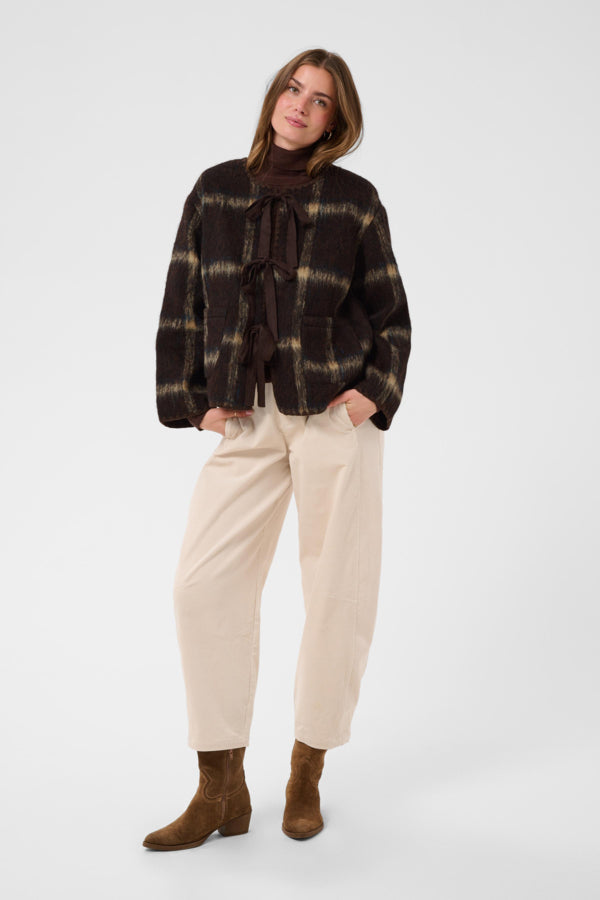 A woman modeling a dark brown and black tie-dye cropped cardigan with a front tie detail, paired with cream-colored trousers and brown suede ankle boots, against a light gray studio background.
