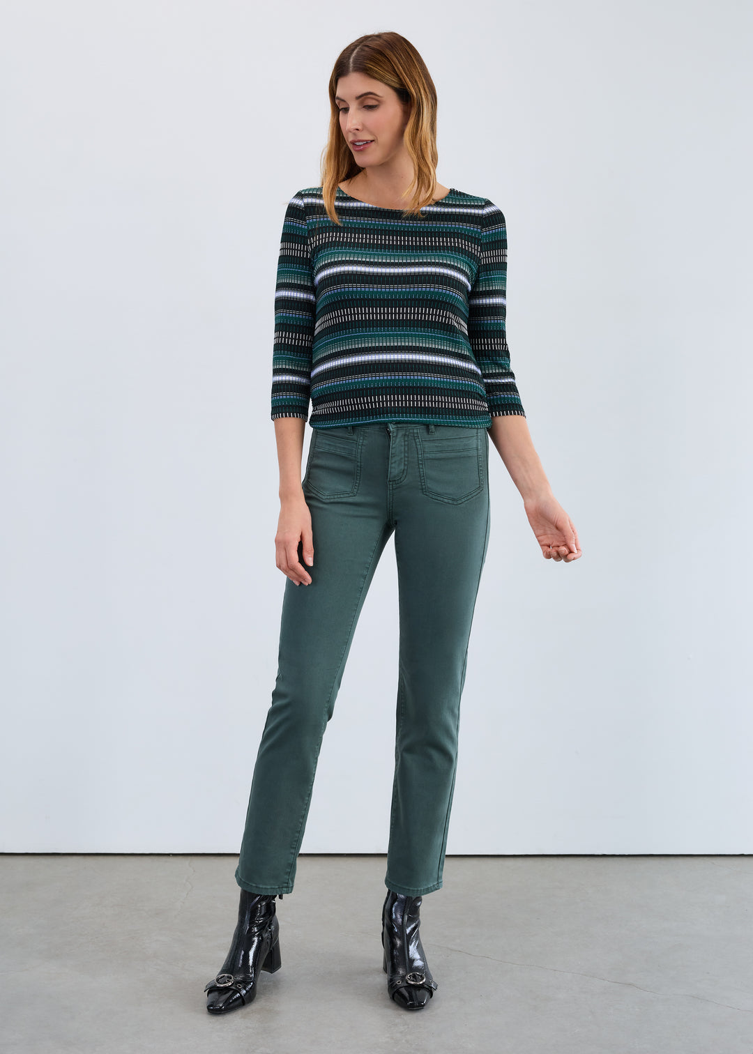 Woman wearing a striped sweater and green pants against a white background