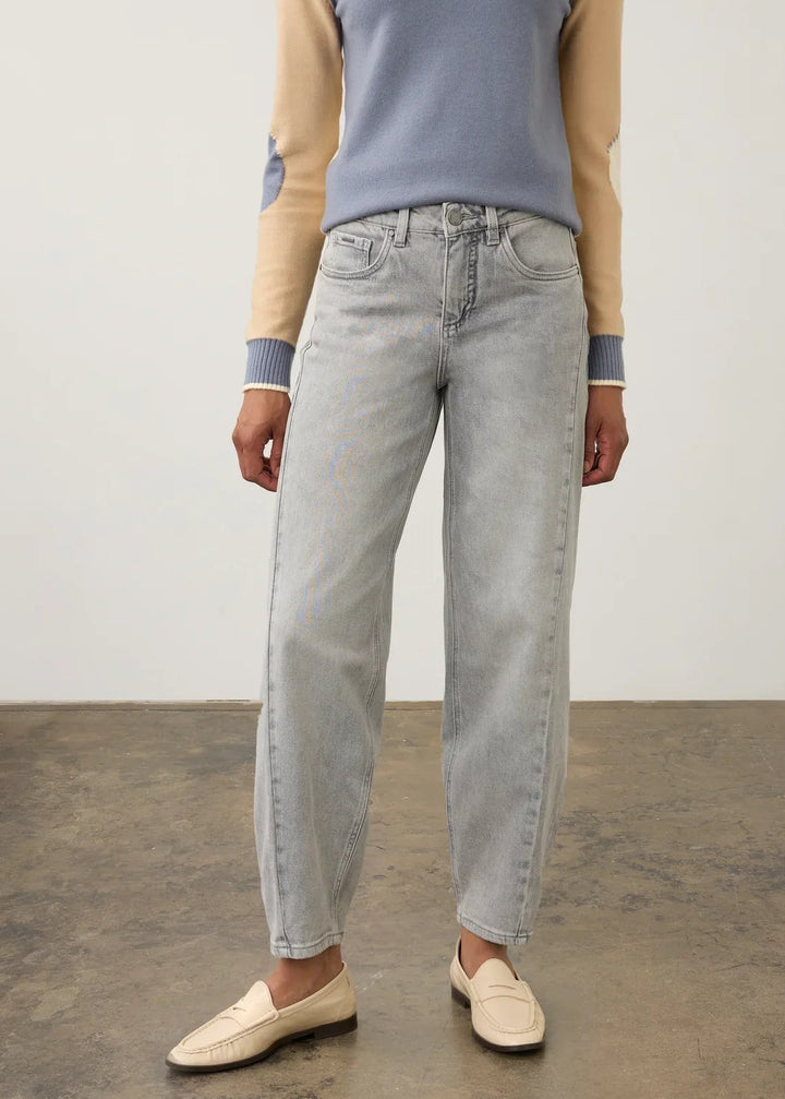 A model wearing a light blue-gray colorblock raglan sweater with beige sleeves, light-wash straight-leg jeans, and cream loafers, standing against a neutral studio background.