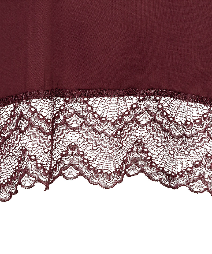 A close-up of a burgundy fabric with a wide, intricate lace hem, shown against a plain white background.