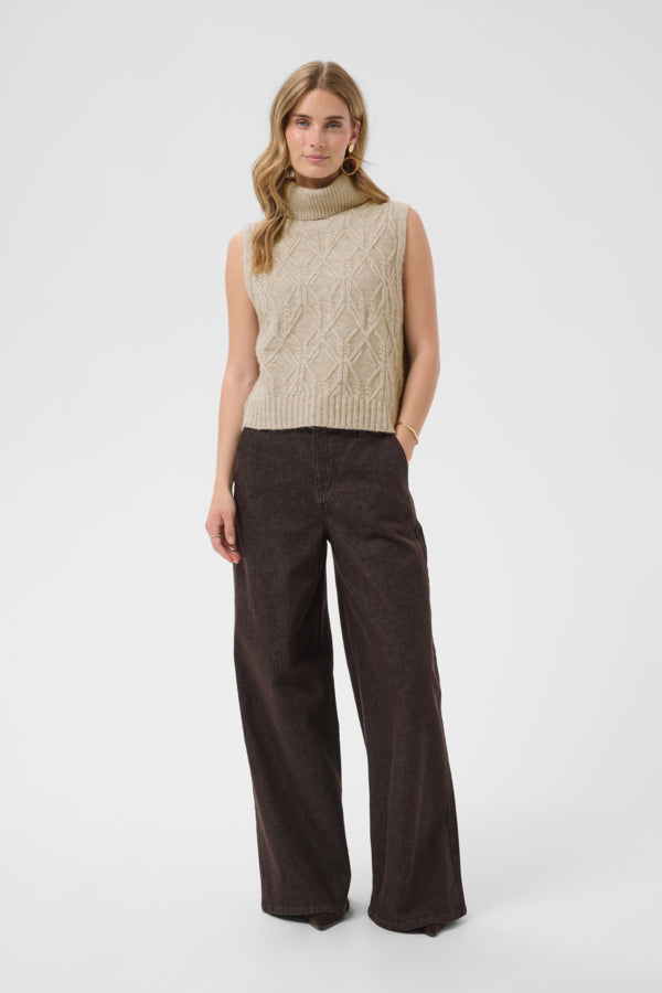 Woman wearing a beige sleeveless knitted top and brown wide-leg pants on a white background