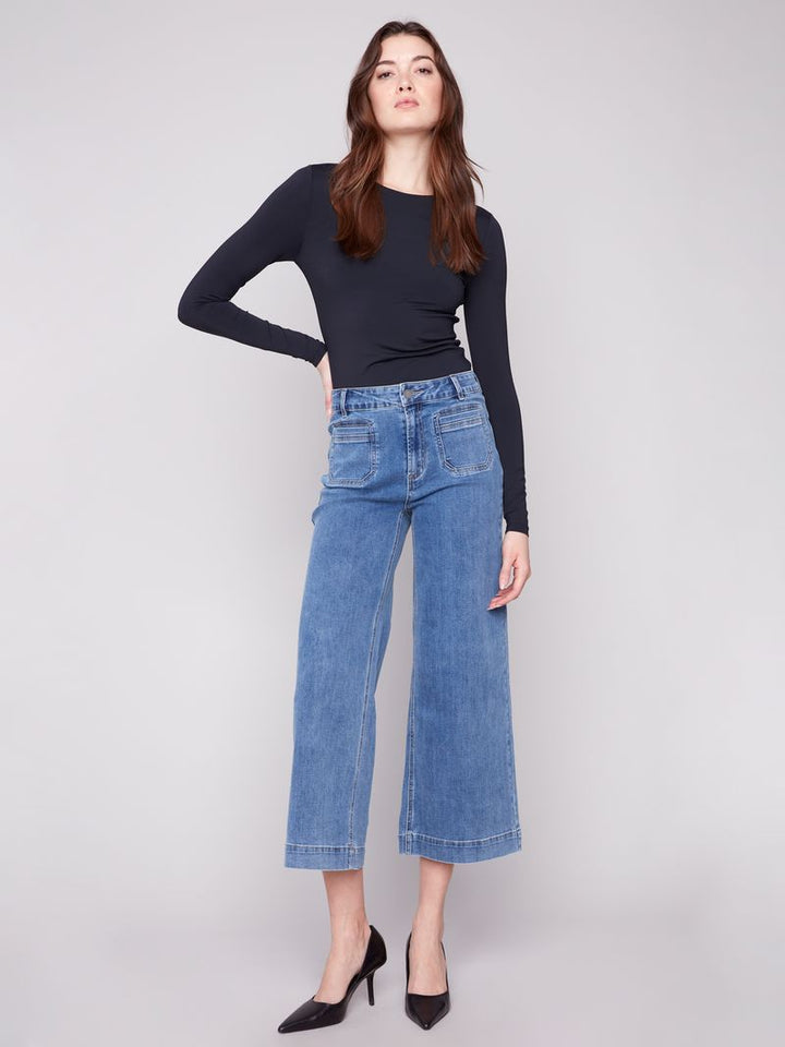Woman wearing blue jeans and a black top on a plain background