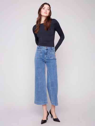 Woman wearing a black long-sleeve top and blue jeans on a white background