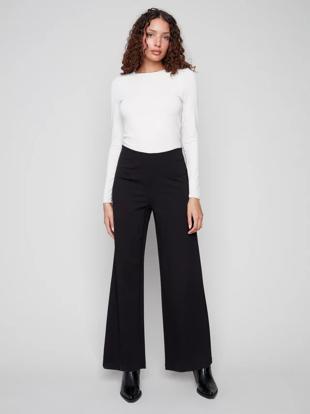 Woman wearing a white top and black pants on a gray background
