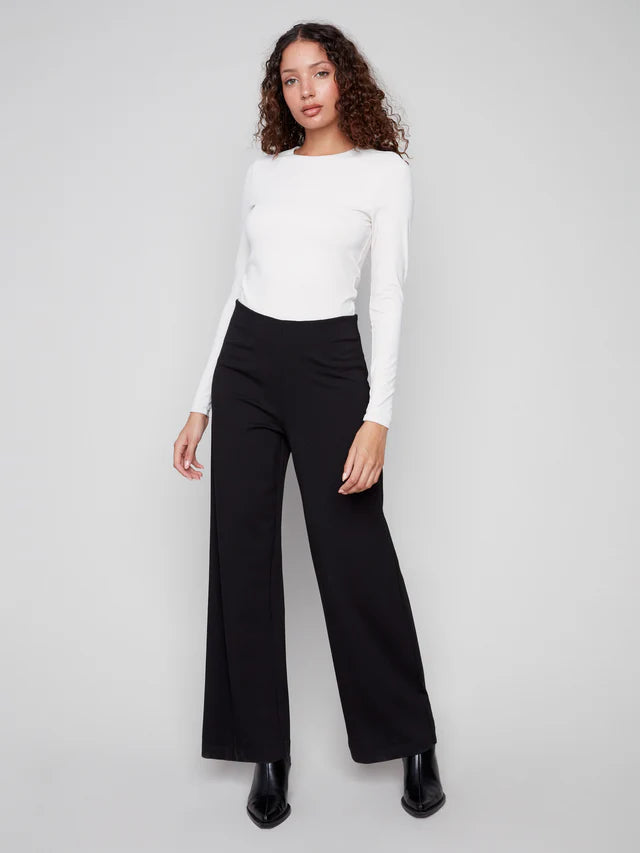 Woman wearing a white top and black pants on a plain background