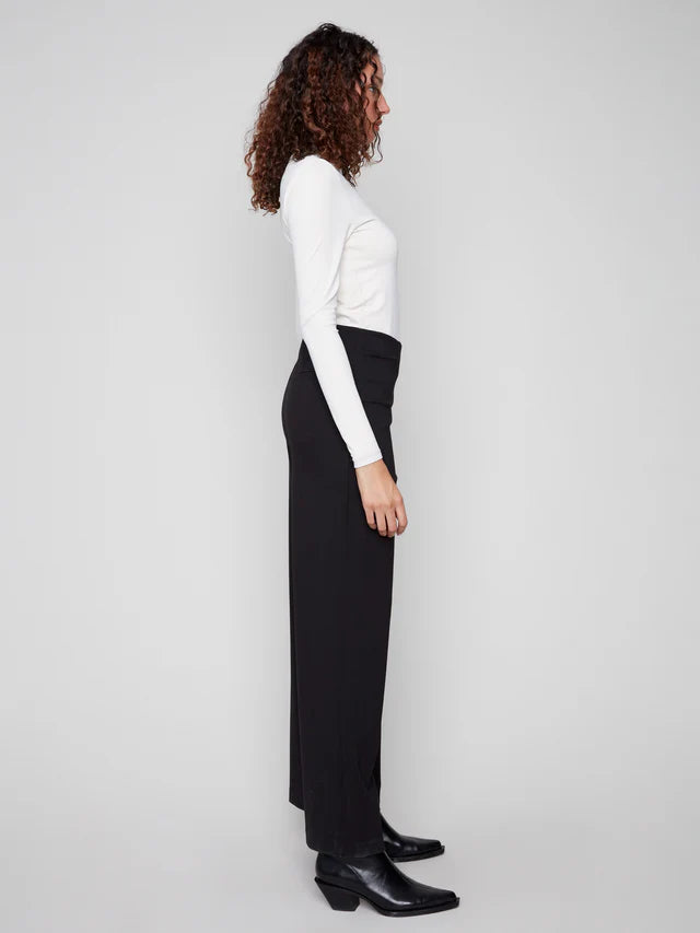 Person wearing a white long-sleeve top and black pants on a plain background