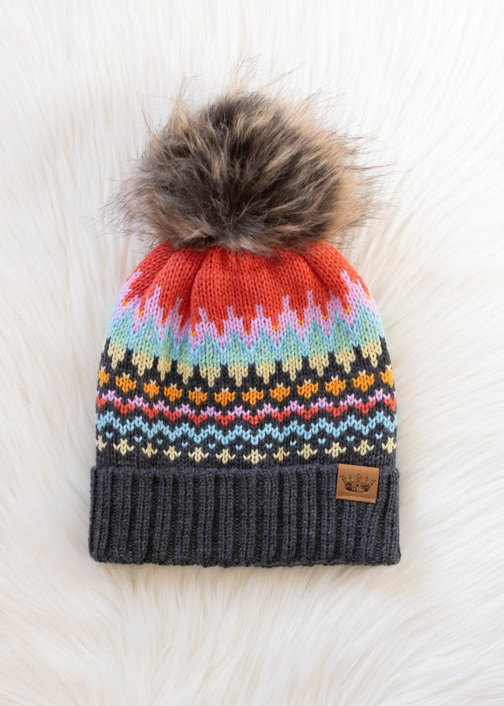 Colorful knit beanie with a fur pom-pom on a white surface