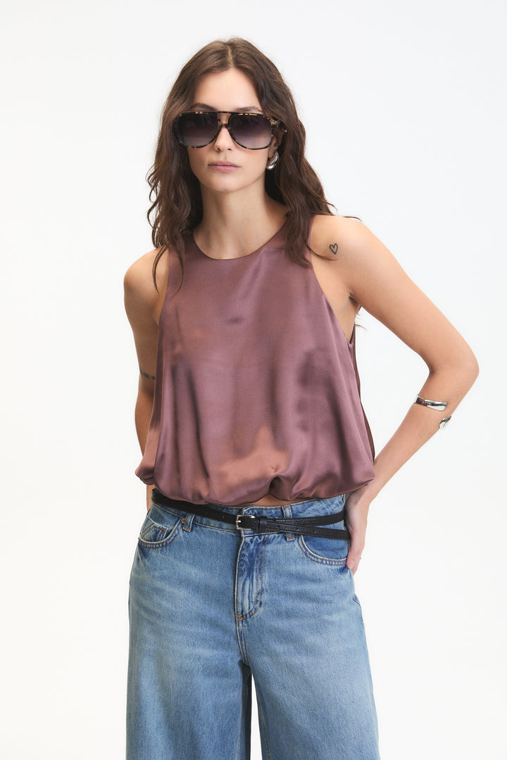 Woman wearing a brown sleeveless top and blue jeans with sunglasses on a white background
