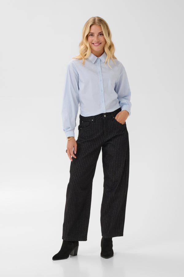 A woman modeling a light blue long-sleeve button-up shirt and black pinstriped wide-leg trousers, paired with black ankle boots, against a plain white studio background.