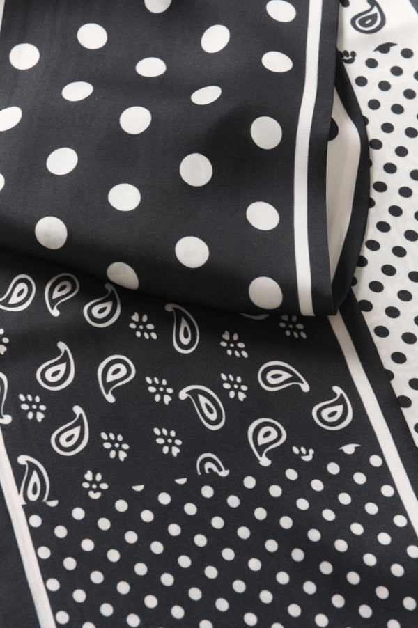Black and white patterned scarf with white polka dots and white paisley motifs on a black background, folded to show its design and border.